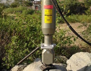 En hydraulisk bergspräckare i arbete på ett stort stenblock utomhus.