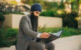 Skäggig man i turban granskar dokument i en portfölj utomhus