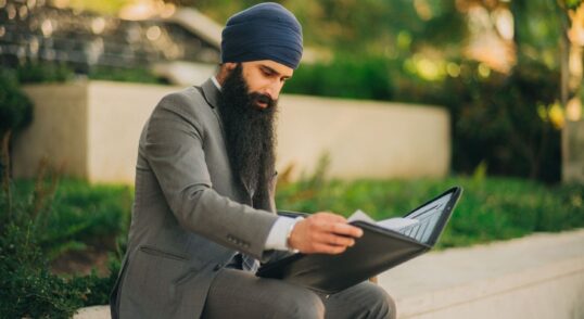 Skäggig man i turban granskar dokument i en portfölj utomhus