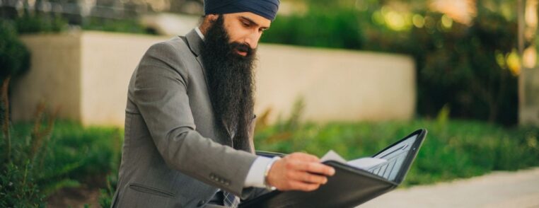 Skäggig man i turban granskar dokument i en portfölj utomhus