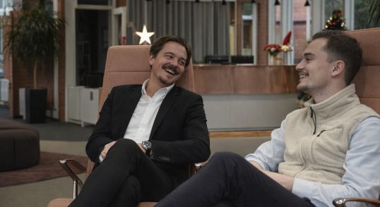 Två kollegor sitter i en lounge och diskuterar kursmarknadsföring via nyhetsbrev.